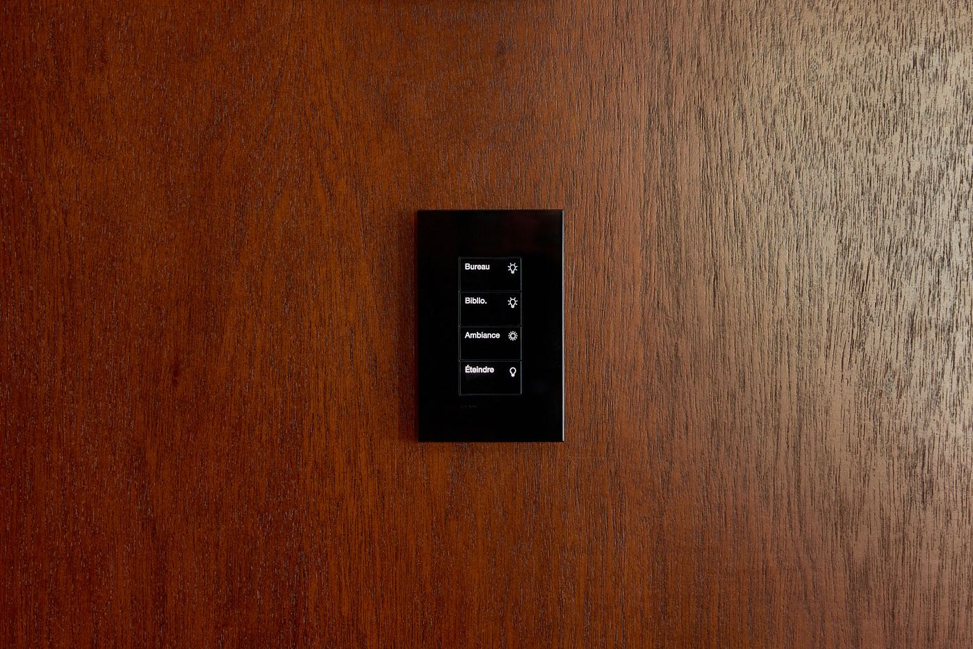 Backlit black Lutron keypad on a dark wood wall
